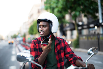 Handsome African man with scooter in the city. Young man talking to the phone.