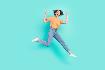 Fototapeta na wymiar Photo of charming sweet young woman dressed striped t-shirt smiling jumping showing v-signs isolated teal color background