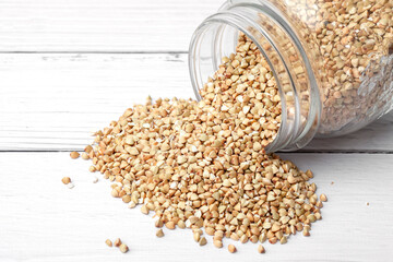 Green buckwheat is poured out of a glass jar onto a white table. Place for text
