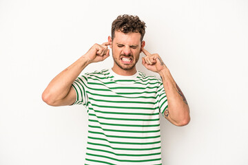 Fototapeta premium Young caucasian man isolated on white background covering ears with fingers, stressed and desperate by a loudly ambient.