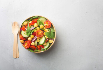 Vegetarian chickpea beans salad prepared with tomatoes and cucumber in a paper bowl with wooden fork
