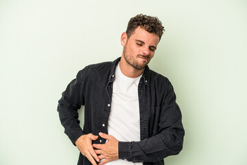 Young caucasian man isolated on green background having a liver pain, stomach ache.