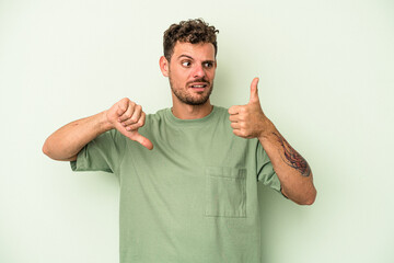 Young caucasian man isolated on green background showing thumbs up and thumbs down, difficult...