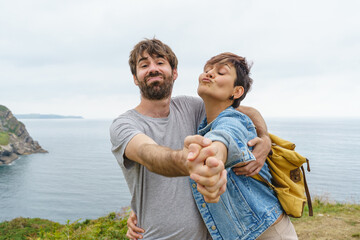 Funny couple in love hugging and dancing on a cliff outdoors. Horizontal view of heterosexual happy couple in holidays. Travel and people concept.