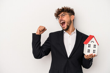 Young arab real estate man holding a model house isolated on isolated background raising fist after...