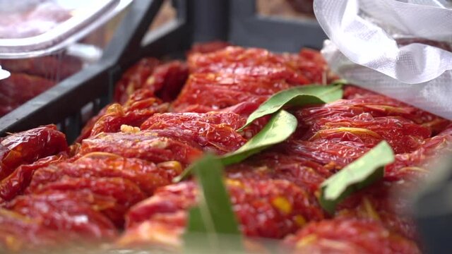 Sun dried tomatoes with fresh herbs and spices selling on the market. Pile of sun dried red tomato halves in the black basket. 