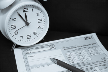 a white alarm clock on which it is 5 to 12 o'clock and a ballpoint pen are lying on a tax return