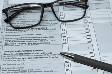 pair of glasses and a ballpoint pen lie on a tax return