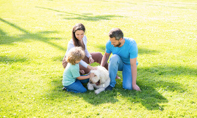 father mother and child on green park grass. friendly family with pet.