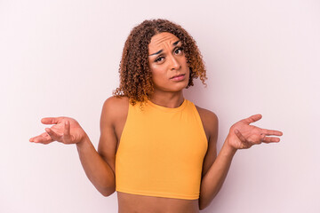 Young latin transsexual woman isolated on pink background doubting and shrugging shoulders in...