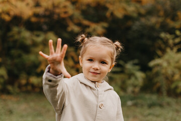 portrait of a little cute girl which shows the palm in the autumn park