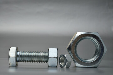 composition of new bolts and nuts of different sizes on a gray background.