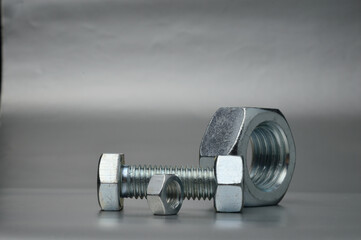 composition of new bolts and nuts of different sizes on a gray background.