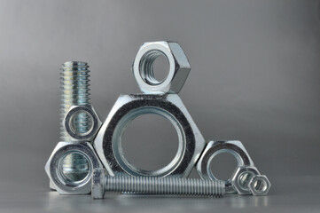 composition of new bolts and nuts of different sizes on a gray background.