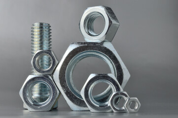 composition of new bolts and nuts of different sizes on a gray background.