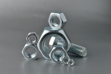 composition of new bolts and nuts of different sizes on a gray background.