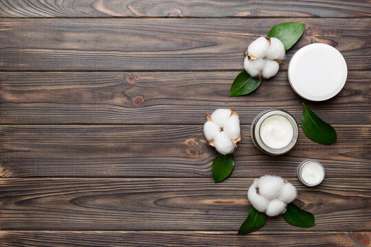 Organic cosmetic products with cotton flower and green leaves on wooden background. Copy space, flat lay
