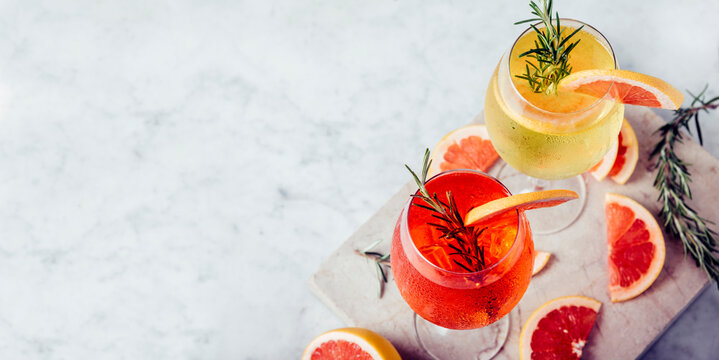 Red and white aperol spritz garnish in wine glasses with rosemary and grapefruit on luxury marble table. Bitter alcohol cocktail in wineglass. Top view. Happy hour restaurant menu banner.