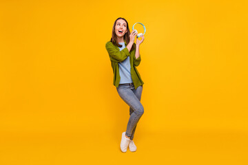 Photo of charming cute young lady wear green shirt holding earphones smiling singing dancing isolated yellow color background