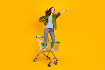 Full length photo of crazy happy young woman look empty space ride trolley isolated on yellow color...