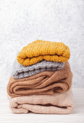 Pile of warm knitted clothes, sweaters and caps on rustic white wooden background. Cozy folded knitwear stack, winter wardrobe capsule concept, shopping 