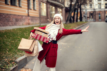 Cheerful girl with a shopping bags trying to catch a taxi at the street near the mall. Happy lifestyle and holiday discounts concept.