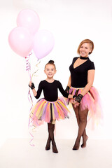 Funny Mother and daughter in same outfits with tutu skirts posing with pink balloons in studio on the white background. Little girl and young mom together