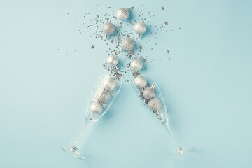 Top view photo of splash of silver christmas decorations from two champagne glasses on isolated pastel blue background