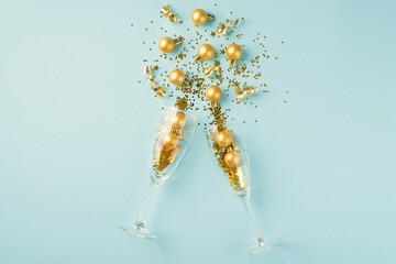 Top view photo of splash of gold christmas decorations from two champagne glasses on isolated pastel blue background - obrazy, fototapety, plakaty