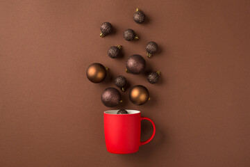 Top view photo of brown and gold christmas tree balls flying out of red cup on isolated brown background