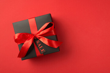 Top view photo of black giftbox with red ribbon bow and tag on isolated red background with text on pricetag