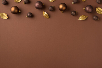 Top view photo of christmas tree decorations brown and gold balls and golden leaves on isolated brown background with copyspace