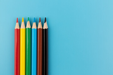 Six colored pencils close-up on a blue background with a copy of the space. The texture of bright colored wooden pencils.