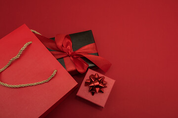Creative look, two red and black gift boxes and a red shopping bag on a red background. Black Friday, discounts, sales, Christmas shopping on a red background, a place for text, a black gift box with