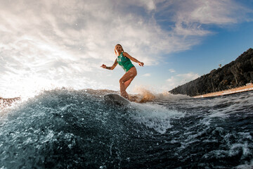 Fototapeta na wymiar athletic woman in a turquoise vest on wakeboard actively riding the river wave