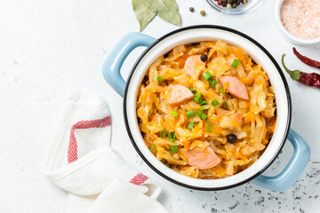 Stewed cabbage with sausages in a pot. Top view, copy space.