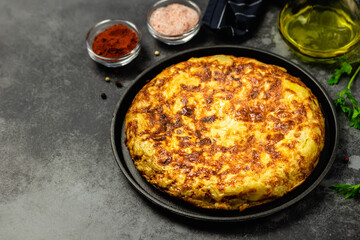 Traditional breakfast Spanish tortilla in cast iron skillet, dark background. Space for text.