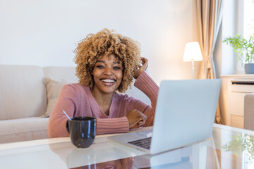 Shot of a young woman using a laptop on the sofa at home. Happy Girl Relaxing on Comfortable Couch and Using Laptop. Young woman working at home