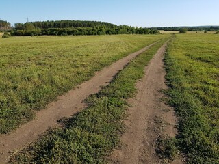 Fototapeta na wymiar Dirt country road in a green field