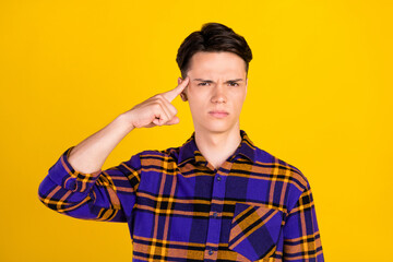 Photo of serious brunet young guy finger head wear checkered shirt isolated on yellow color...