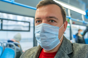 Fototapeta na wymiar Portrait of male passenger wearing medical face mask in public transportation. Millennial man looking away at window, thinking, going to work by bus during coronavirus pandemic. Themes social distance