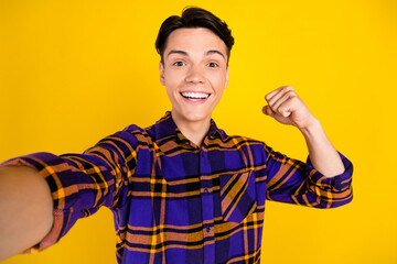 Photo of lovely brunet millennial guy show biceps do selfie wear checkered shirt isolated on yellow color background