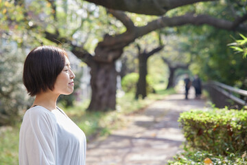 早朝の新緑の中でほほ笑む40代日本人女性