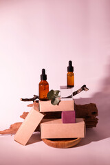 Serum on a podium made of cardboard boxes on a pink background with tree branches. Front view