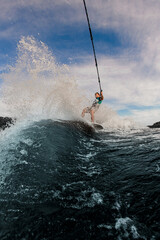Fototapeta na wymiar view of great splashing wave and man holds rope and glides on the waves on the wakesurf board