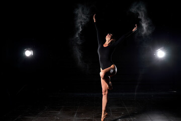 Ballerina dancing with flour on black studio background. Dancer in black bodysuit dancing...