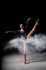 Naklejka premium Dancer posing dancing gracefully in studio with cloud of dust, flour. flexible Dancer in black suit is moving, in action, having good choreographic training, raising leg up. ballet, performance