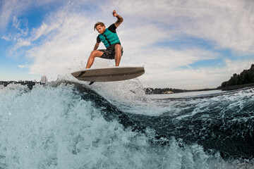 Energy man wakesurfer skillfully jump up over splashing wave against cloudy sky