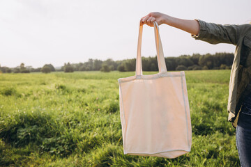 Young blonde woman with white cotton bag in her hands on nature background. Empty reusable canvas...