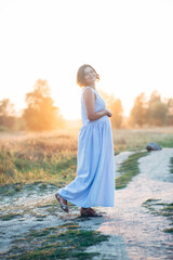 Portrait of happy pregnant woman in park at sunset with warm backlight in the background